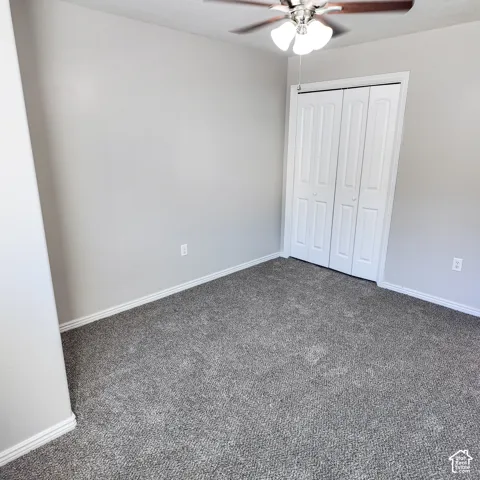 Neutral wall paint, gray carpeting, a ceiling fan with integrated lighting, and bi-fold closet doors