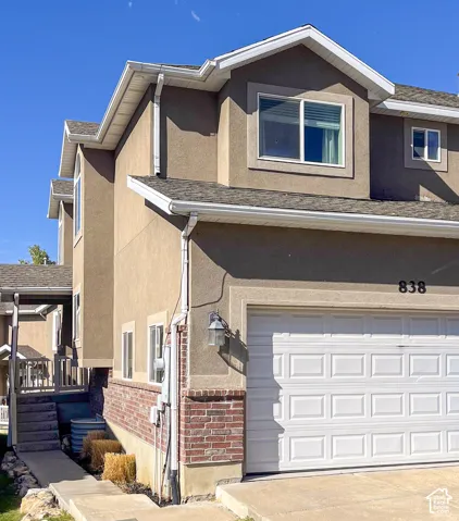 Stucco exterior with brick detailing, white panel garage door, upper-level windows, and white rain gutters