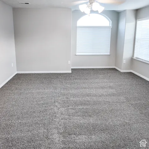 Carpeted room featuring a ceiling fan with integrated lighting, an arched window, and additional windows with blinds
