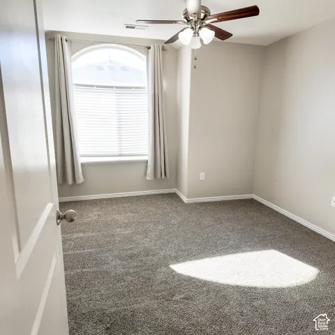 Arched window with blinds, ceiling fan with light fixture, neutral wall paint, and gray carpeting