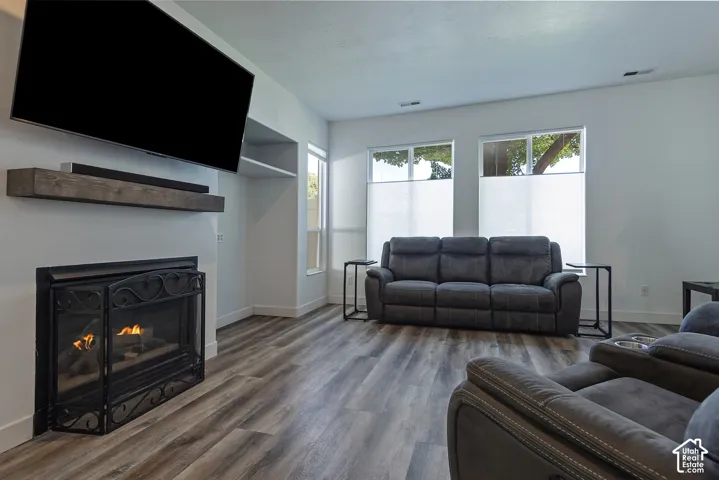 Wood-finish flooring, built-in shelving, multiple windows with privacy blinds, and a fireplace with a decorative screen