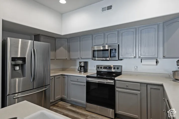 Stainless steel appliances, wood-finish flooring, gray cabinetry, built-in microwave, and solid surface countertops