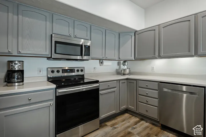 Gray cabinetry with brushed nickel hardware, stainless steel appliances, light-toned countertops, and wood-finish flooring