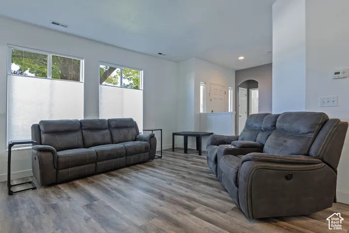 Wood-finish flooring, white walls, arched entryway, recessed lighting, and ample natural light from multiple windows