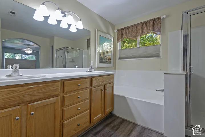 Dual vanity with light wood-finish cabinetry, built-in soaking tub, separate glass-enclosed shower, wood-finish flooring, and a large window
