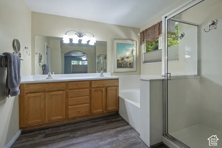 Dual sink vanity with wood-finish cabinetry, a large wall-mounted mirror, and a fixed glass shower enclosure