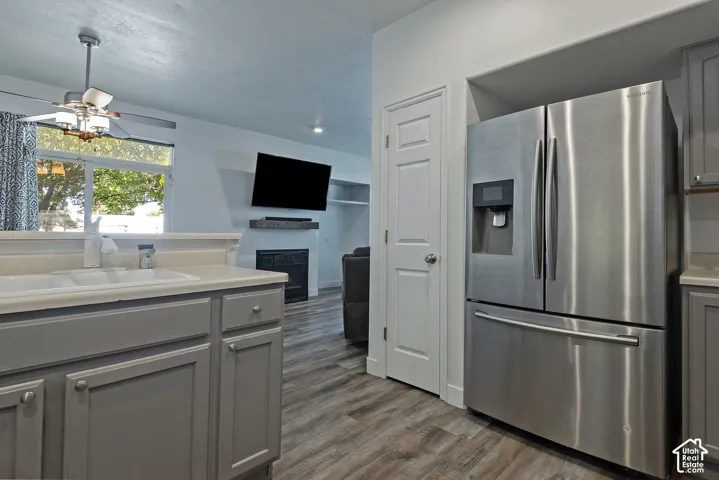 Stainless steel French door refrigerator, wood-finish flooring, white double basin sink, gray cabinetry, and a built-in fireplace