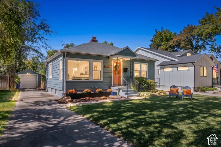 Paved driveway leading to a detached garage, established front lawn, and front porch with steps and railing