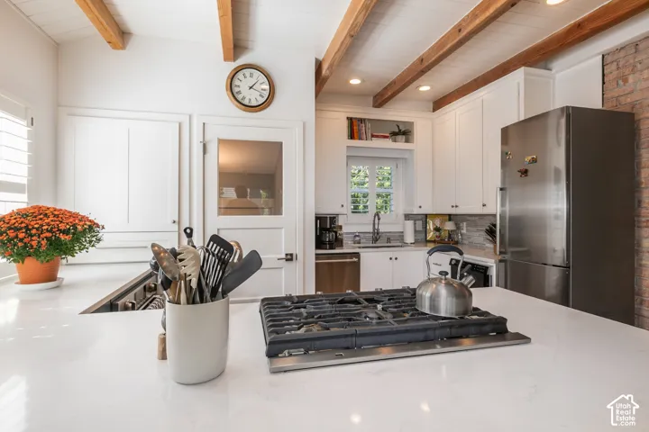 Kitchen featuring white shaker cabinetry, stainless steel appliances, exposed brick accents, and wood-beam ceilings