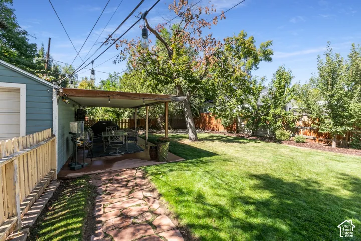Expansive lawn area with mature trees, stone pathway, and covered patio with string lighting