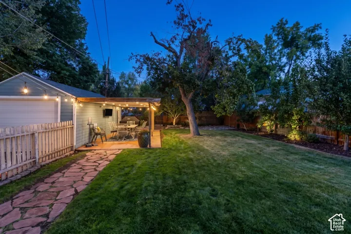 Expansive backyard featuring a stone pathway, manicured lawn, wood picket fence, and a covered patio structure