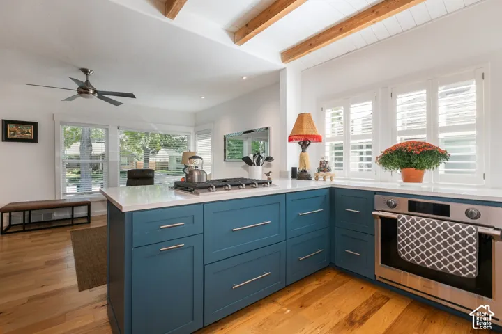 Kitchen featuring wood-finish flooring, exposed wooden ceiling beams, white cabinetry, a built-in stainless steel oven, and a gas range