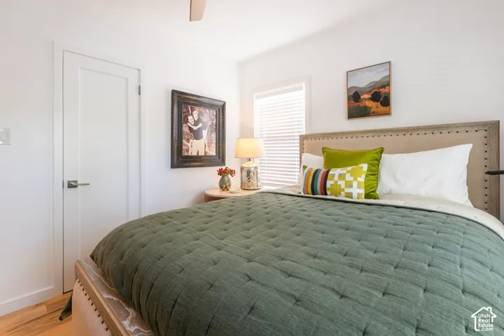 White walls, wood-finish flooring, white door with brushed nickel hardware, window with white blinds, and a ceiling fan