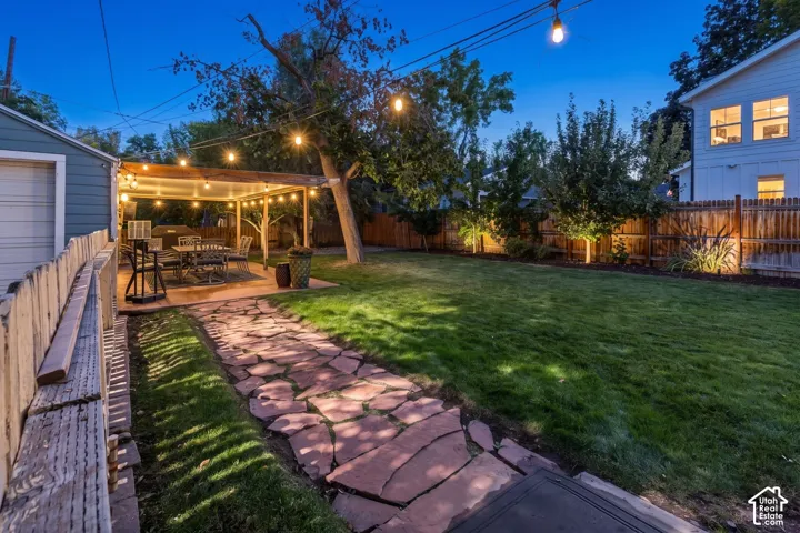 Expansive backyard featuring a stone pathway, a covered patio, a manicured lawn, and perimeter fencing