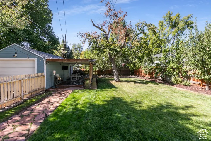 Expansive backyard featuring a stone-paved path, a dedicated patio with a wood pergola, and mature trees