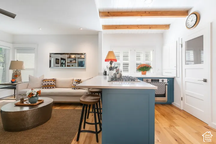 Kitchen with wood-finish flooring, exposed wood beams, and a blue island with a white countertop