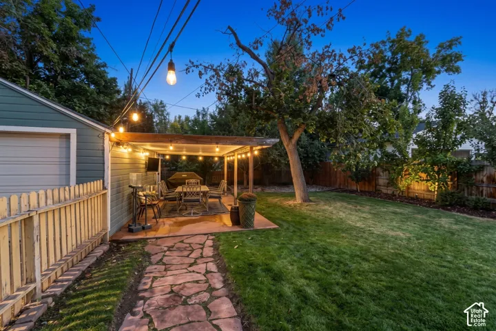 Expansive lawn area with mature trees, a stone-paved walkway, and a covered patio with string lighting