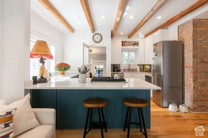 Kitchen featuring exposed ceiling beams, white cabinetry, a stainless steel refrigerator, and a kitchen island with a white countertop and blue paneling