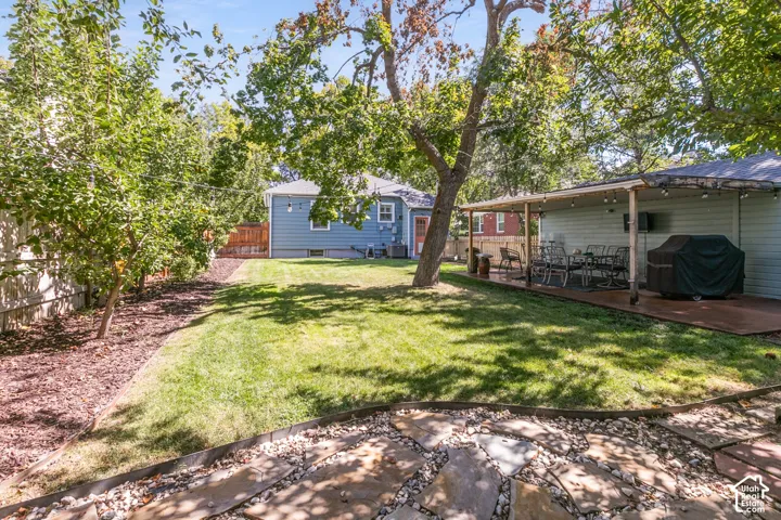 Expansive backyard featuring a manicured lawn, established trees, flagstone patio, and a covered outdoor entertaining area