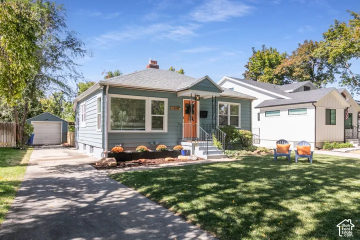Light blue siding exterior with a contrasting orange front door, a front porch with dark railings, a well-maintained lawn, and a paved driveway leading to a detached garage