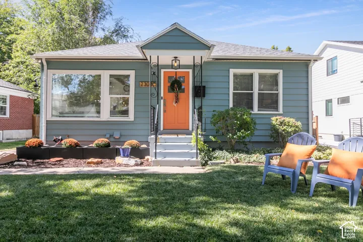 Exterior featuring blue siding, white trim, a vibrant orange entry door, a covered entry porch, and a well-maintained lawn