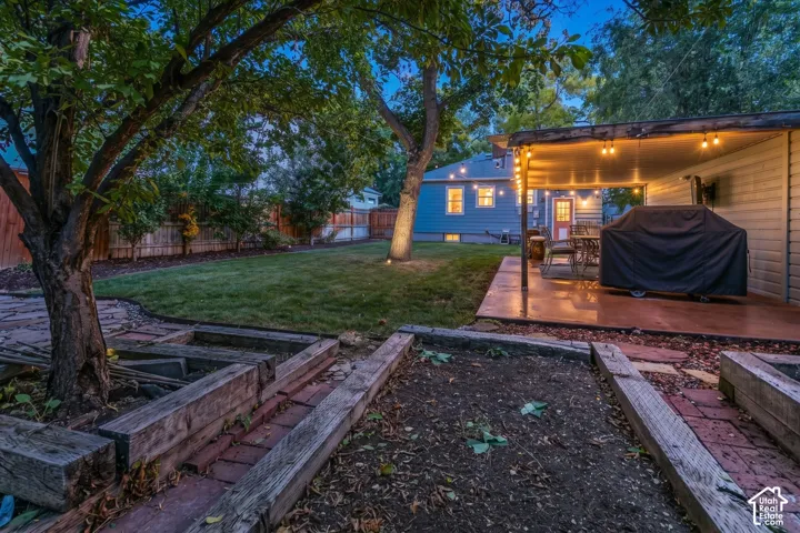 Expansive backyard featuring a manicured lawn, stone paver patio, wood beam garden beds, and mature trees