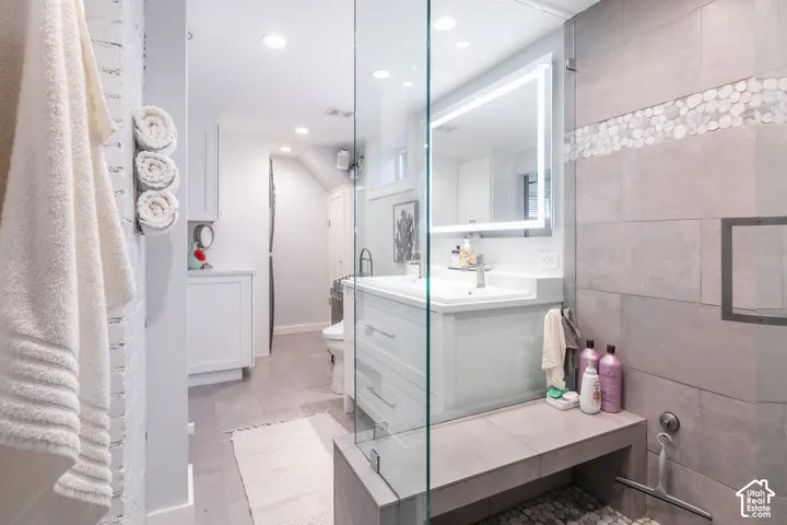 Glass-enclosed shower with a built-in bench, lighted vanity mirror, white vanity with an integrated sink, and recessed lighting