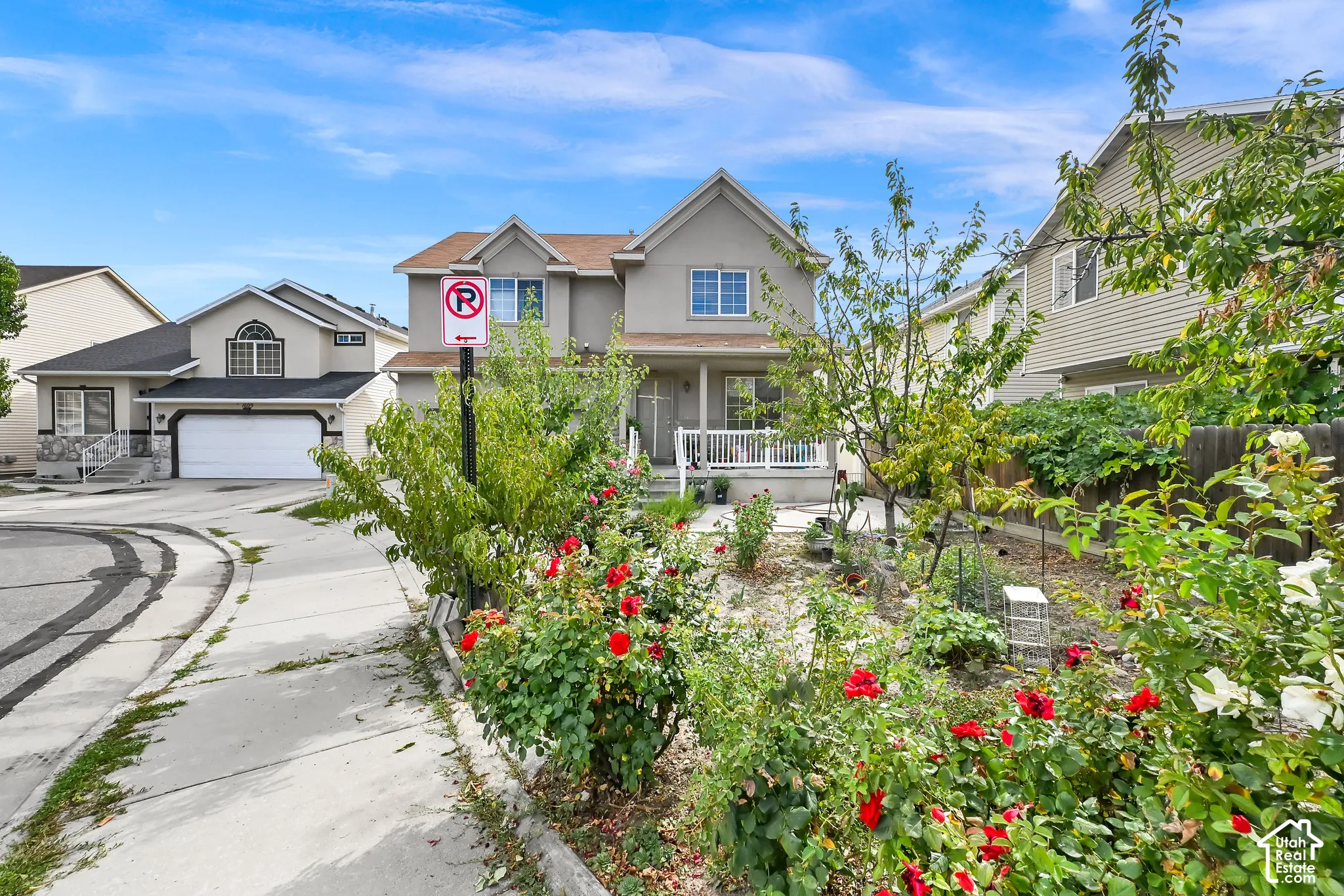 Two-story property with a light-colored exterior and white trim, featuring a covered front porch and mature landscaping with red roses