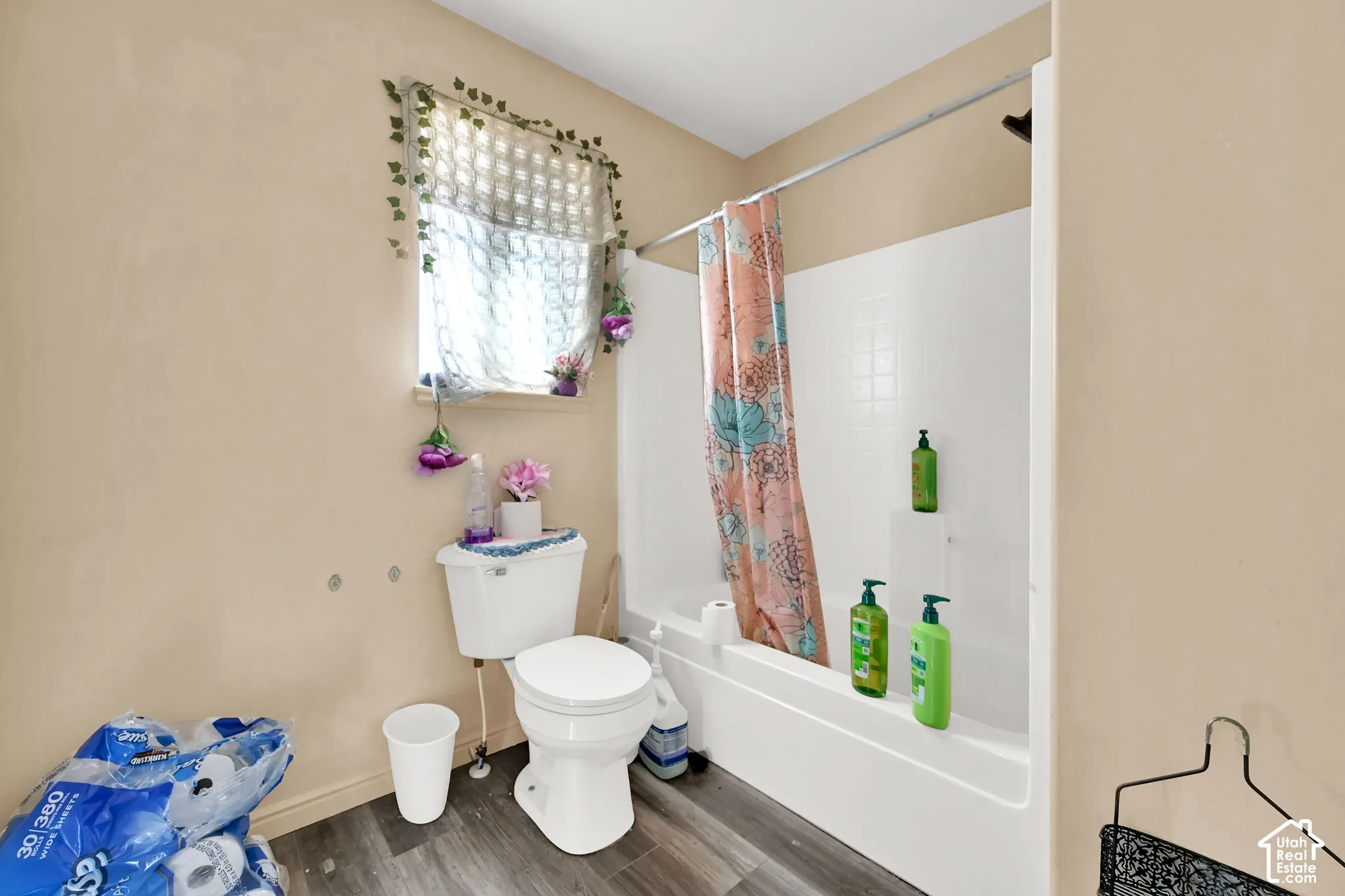Shower-over-tub combination with white tile surround, white toilet, and wood-finish flooring