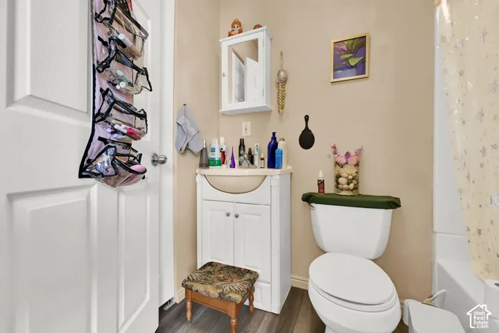 White bathroom vanity with integrated sink, wood-finish flooring, white toilet, and wall-mounted medicine cabinet