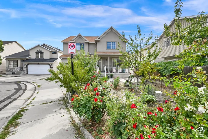 Two-story property with a light-colored exterior and white trim, featuring a covered front porch and mature landscaping with red roses