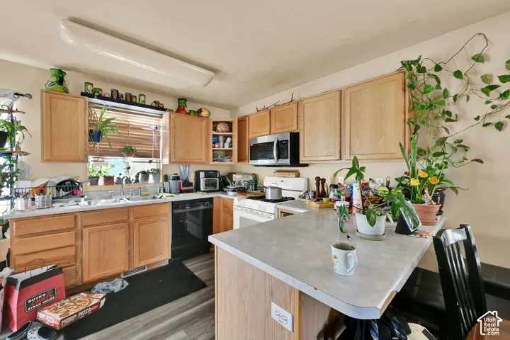 Kitchen featuring wood-finish cabinetry, stainless steel microwave, black dishwasher, and a center island with countertop seating