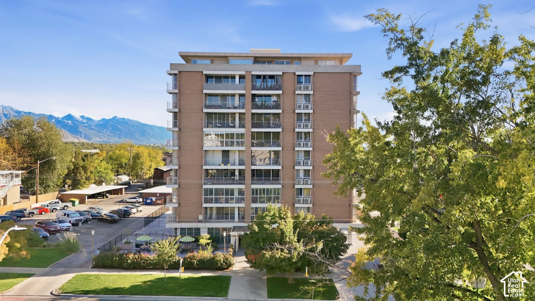 Multi-story building featuring a brick facade, private balconies, and an adjacent paved parking area