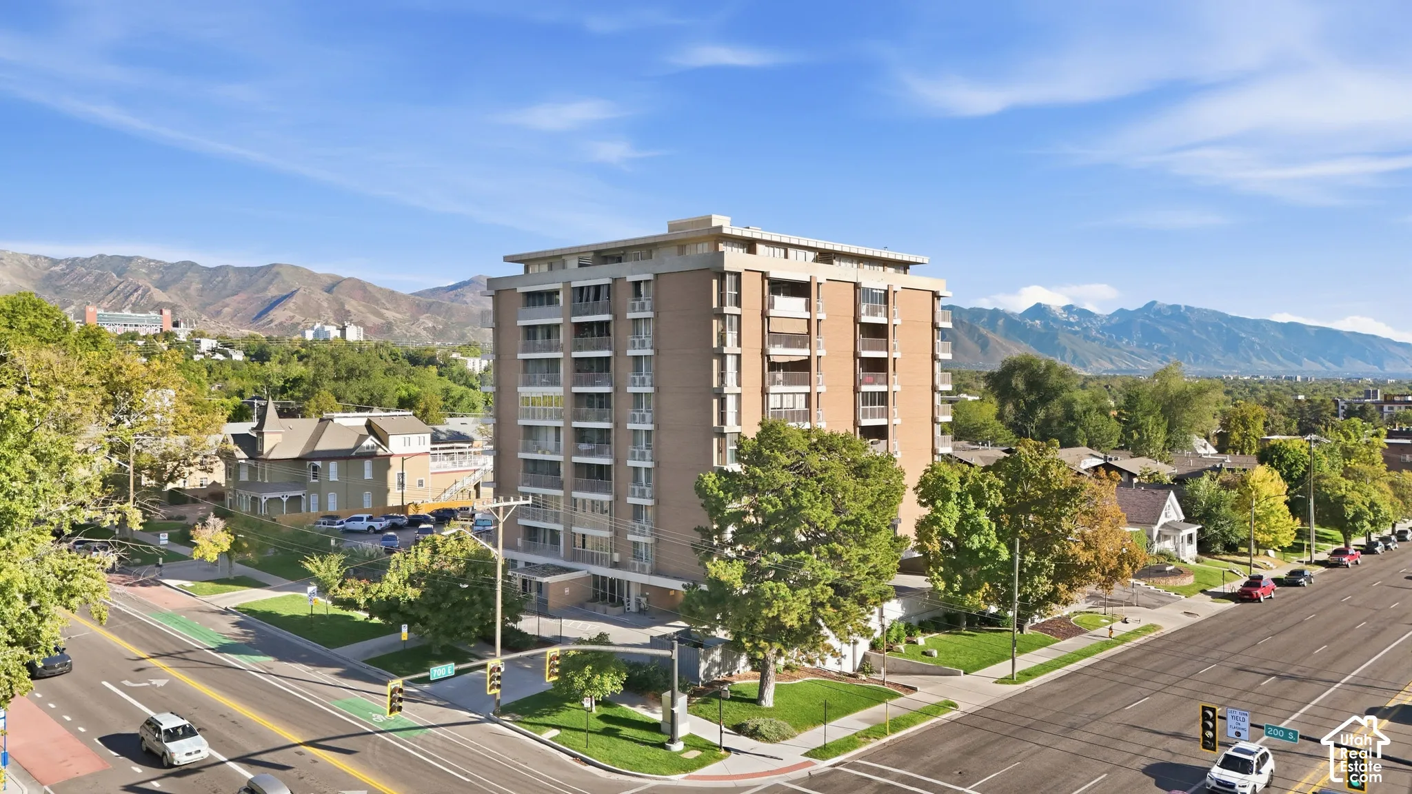 Multi-story brick facade building featuring multiple balconies, surrounding green spaces, and a prominent mountain backdrop