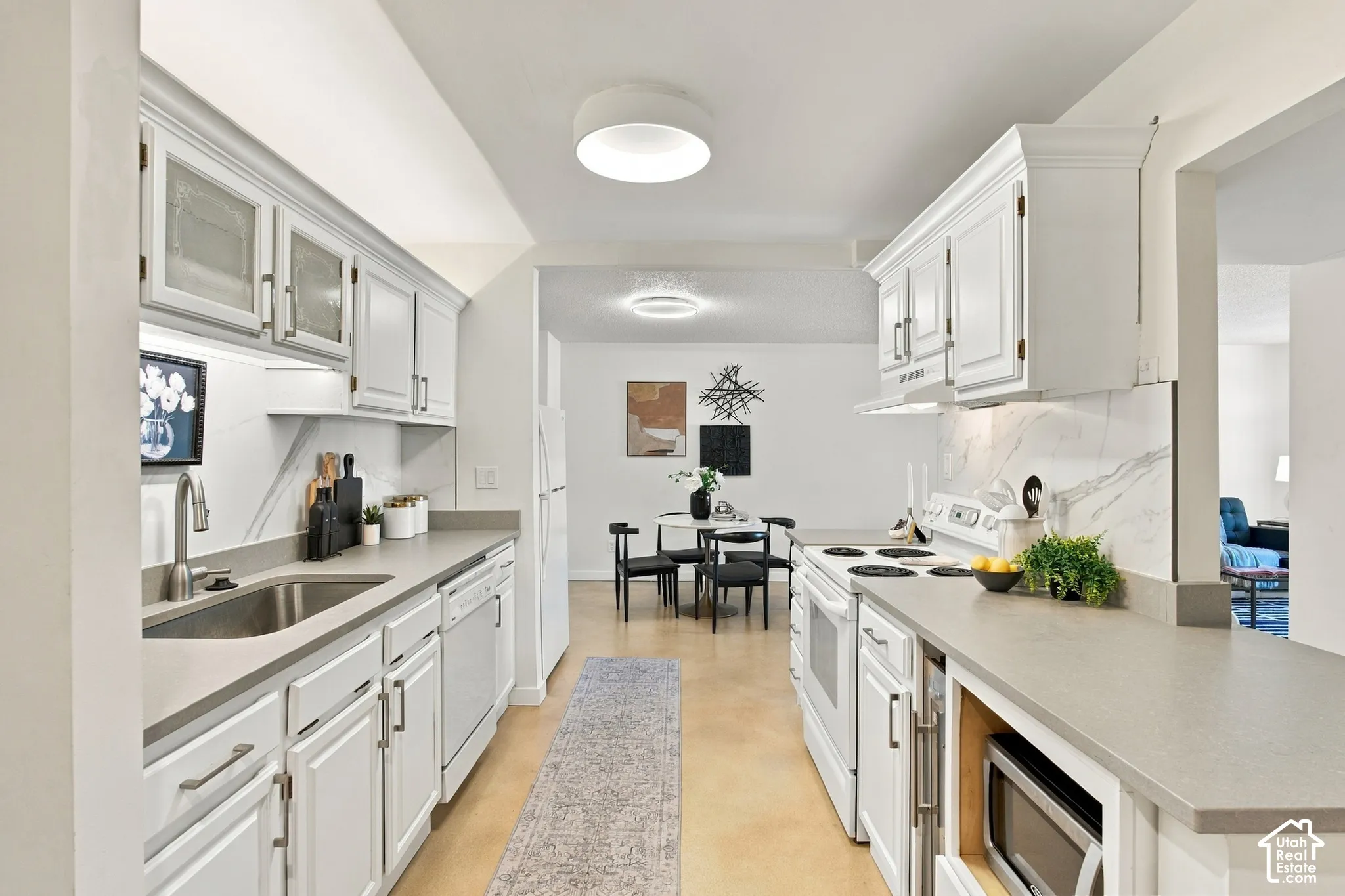 Galley kitchen with white cabinetry, stainless steel sink, integrated appliances, and light-toned countertops