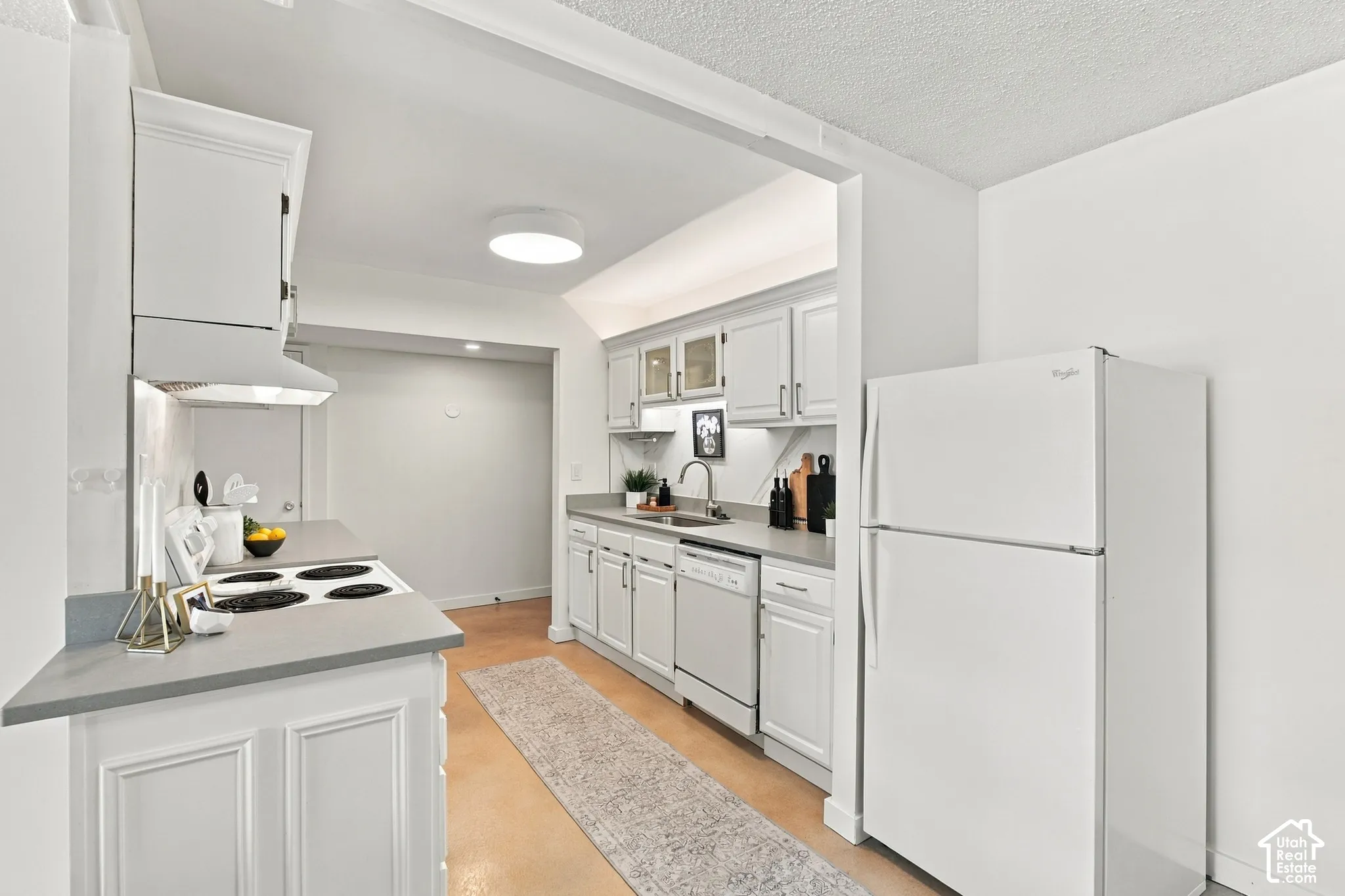 White cabinetry, gray countertops, recessed lighting, and a white refrigerator