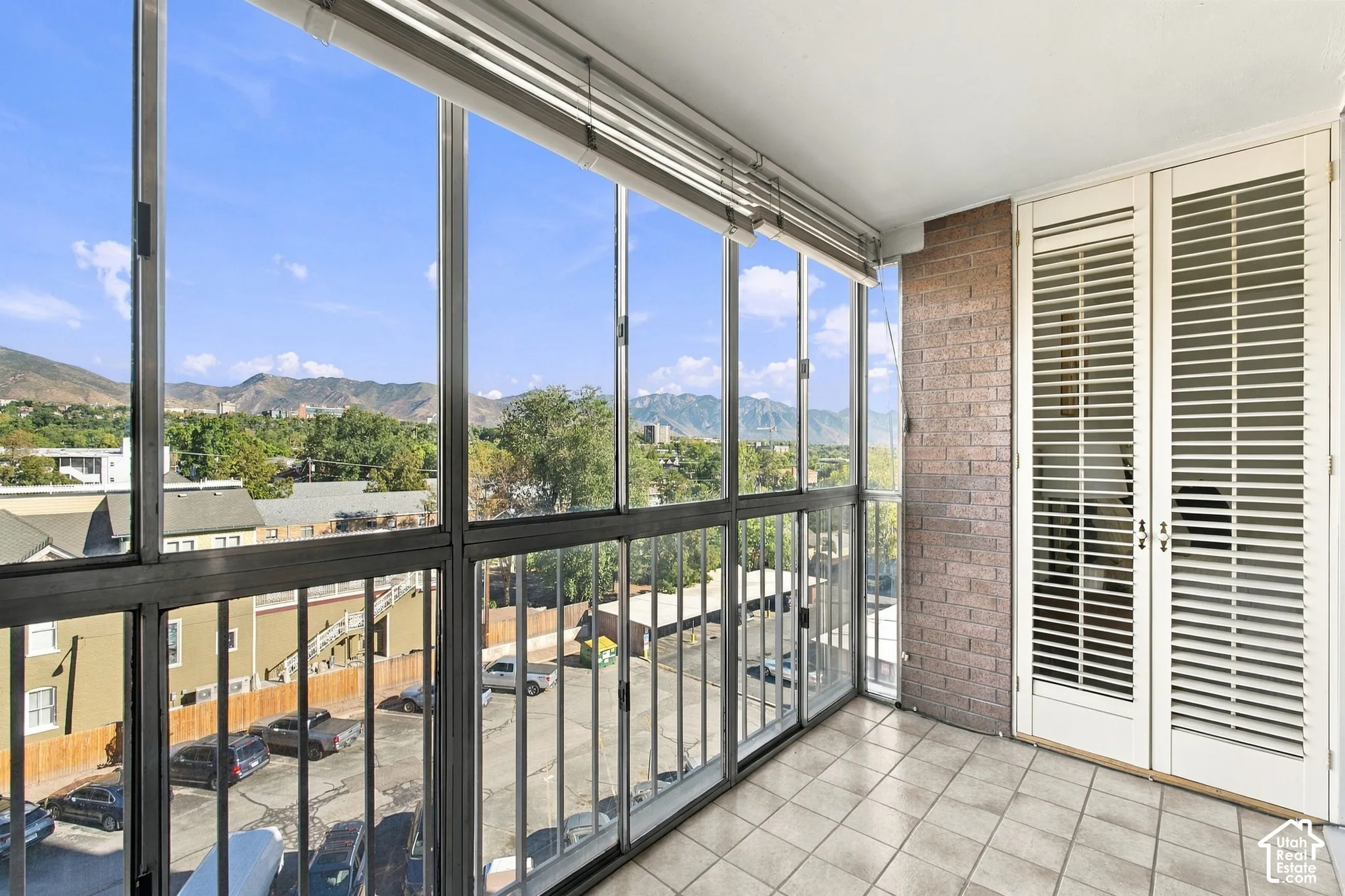 Enclosed balcony featuring floor-to-ceiling windows, tiled flooring, exposed brick wall, and louvered double doors