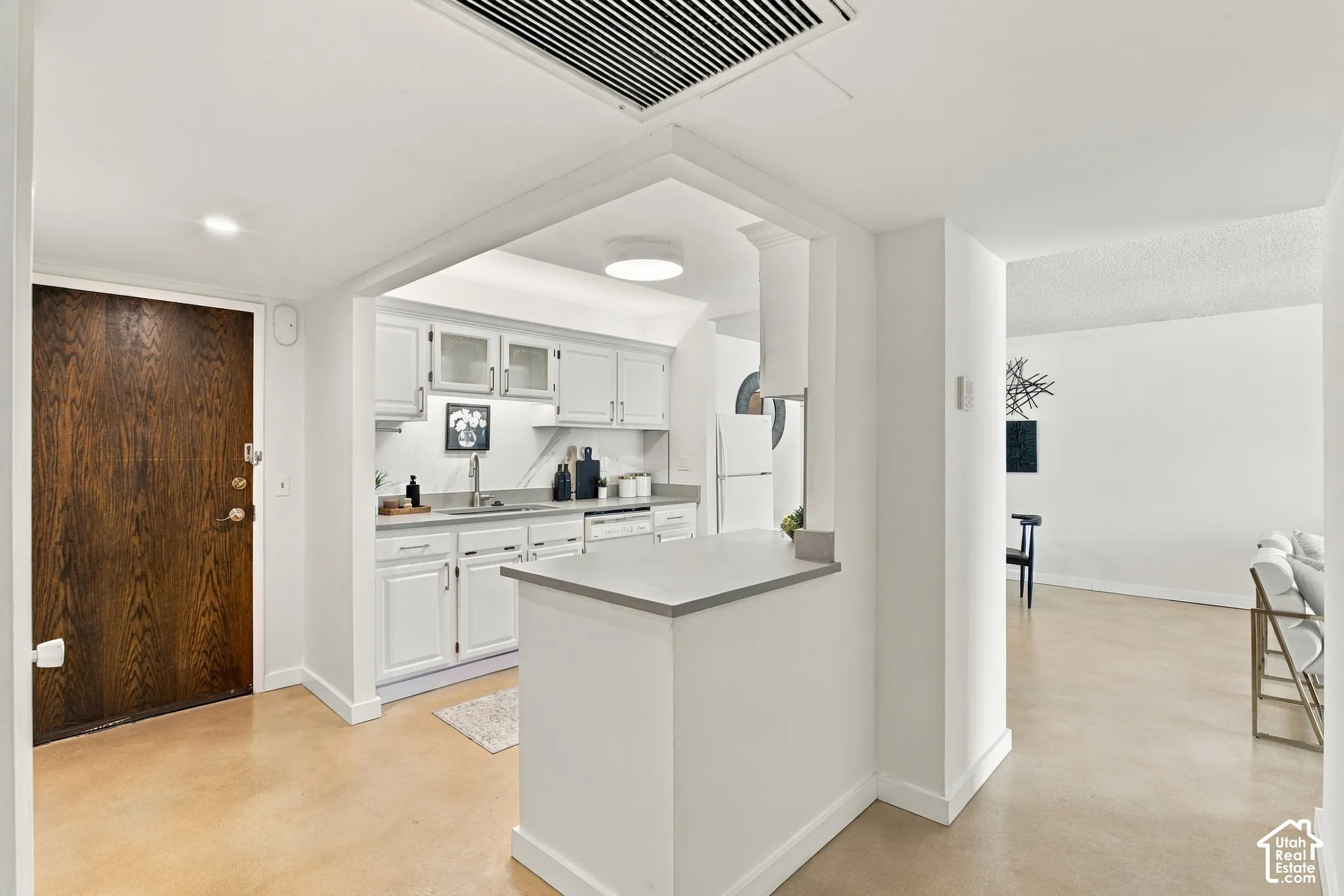 White kitchen cabinetry with glass-front upper cabinets, stainless steel sink, and light-toned countertops