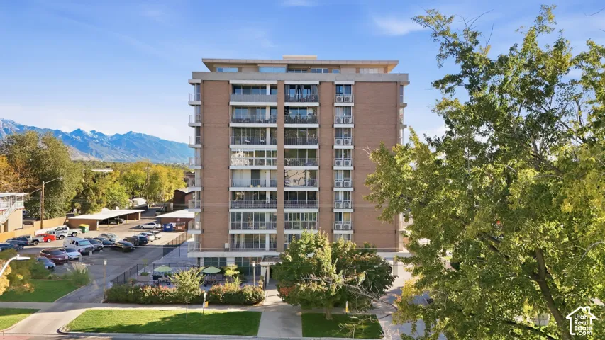 Multi-story building featuring a brick facade, private balconies, and an adjacent paved parking area