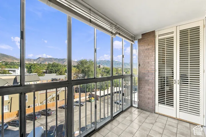 Enclosed balcony featuring floor-to-ceiling windows, tiled flooring, exposed brick wall, and louvered double doors