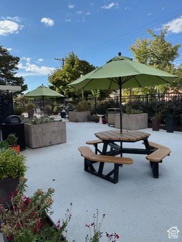 Paved outdoor area featuring decorative planters, a picnic table, bbq, and shade umbrellas