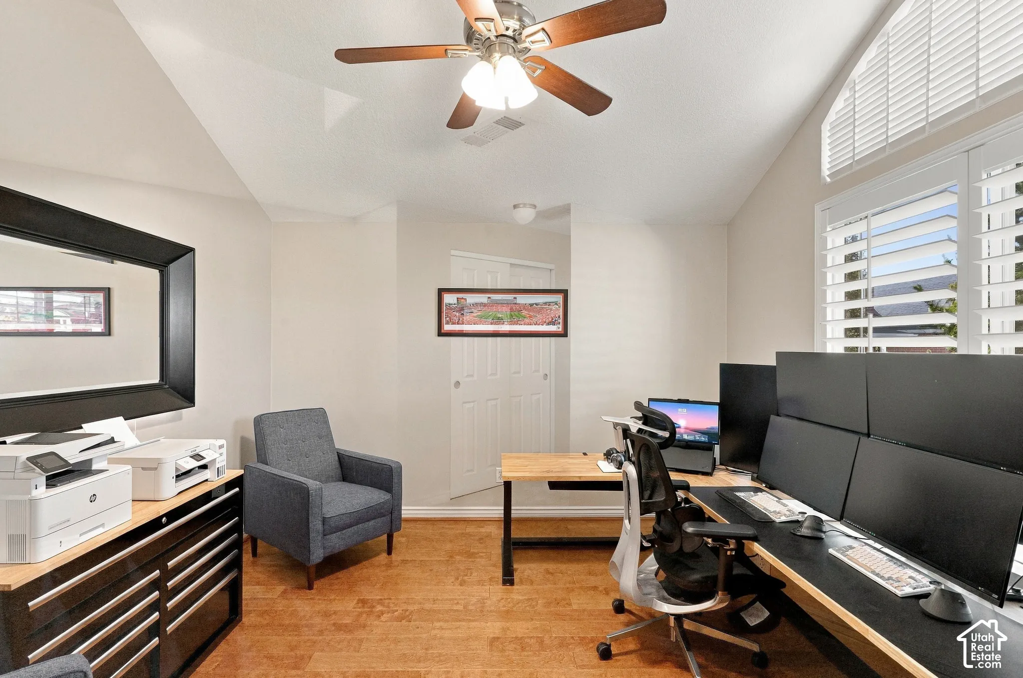 Vaulted ceiling with a ceiling fan, wood-finish flooring, and a window featuring plantation shutters