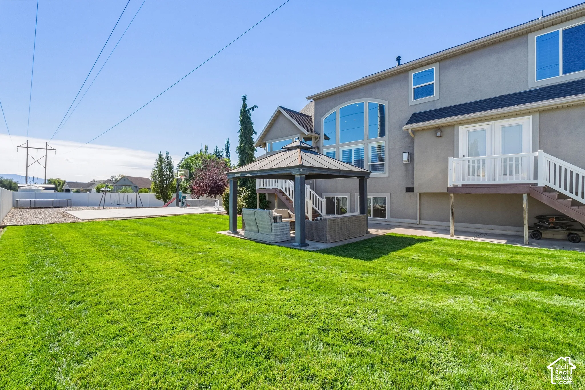 Expansive backyard featuring a manicured lawn, a built-in gazebo, and a hardscaped court