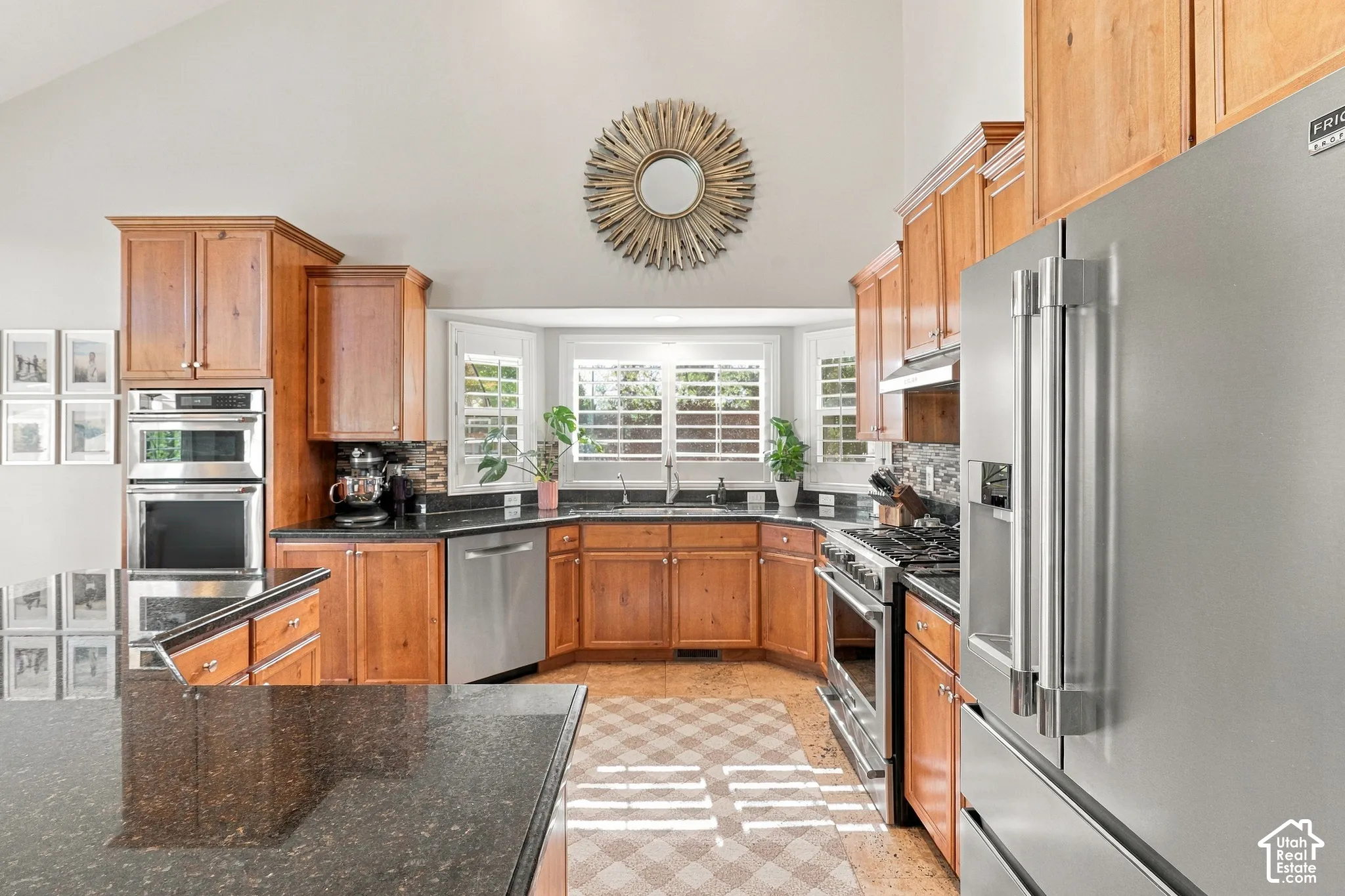 Kitchen featuring wood cabinetry, stainless steel appliances, dark countertops, a tile backsplash, and a bay window
