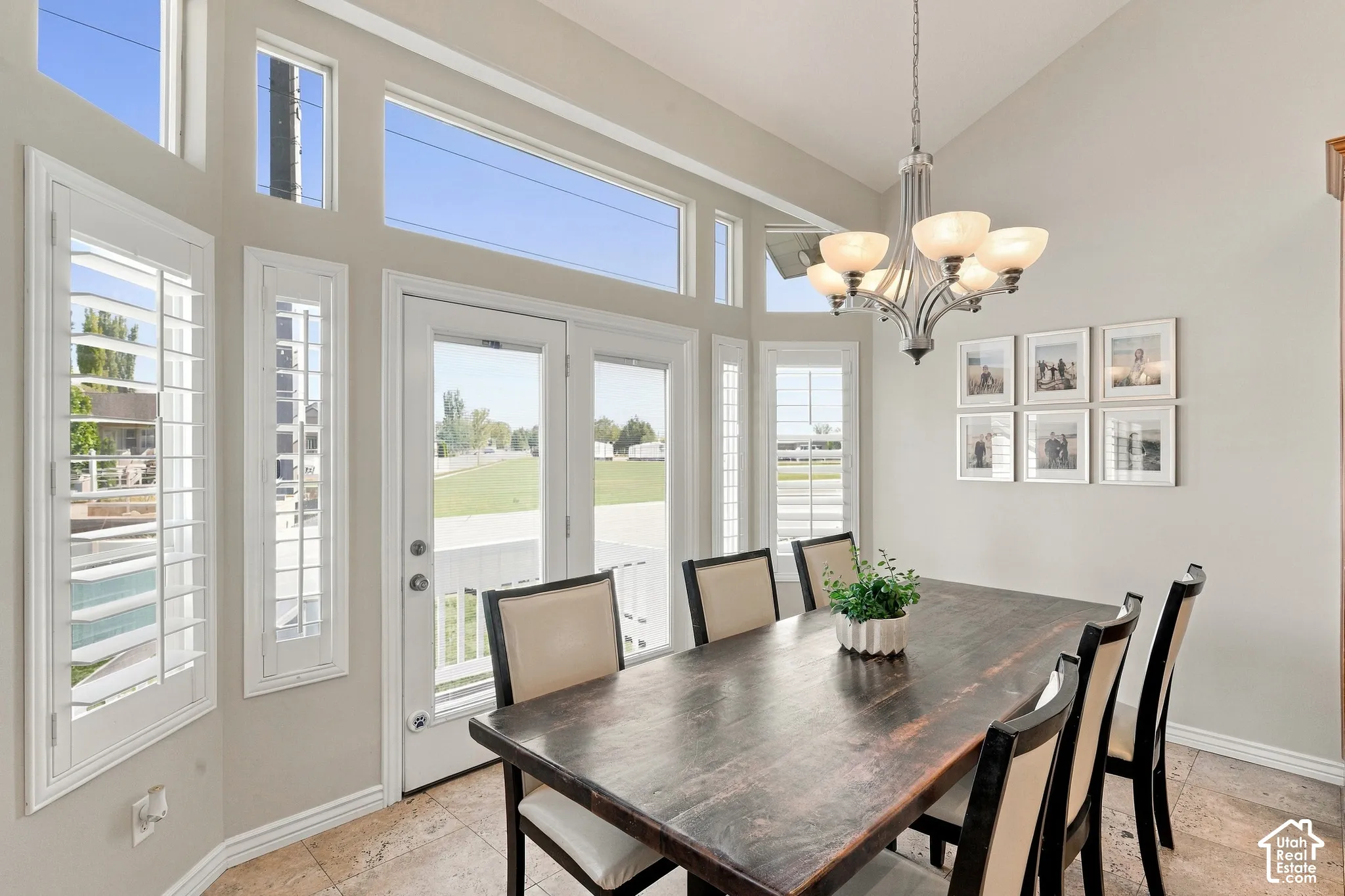 Vaulted ceiling with an ornate chandelier, multiple large windows, and patio door access