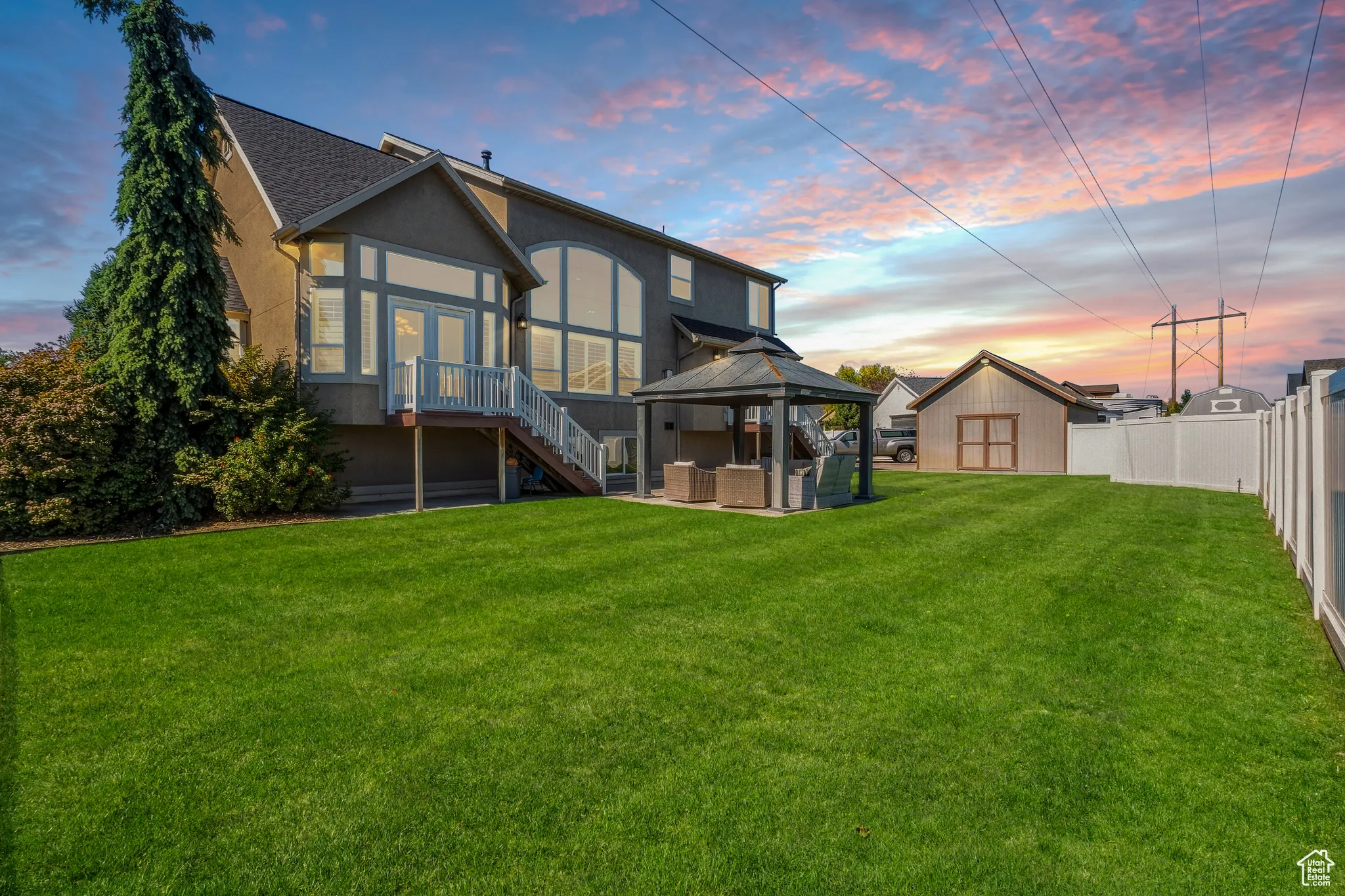 Expansive backyard featuring a manicured lawn, a detached storage shed, a white privacy fence, a covered patio area, and a large deck with steps