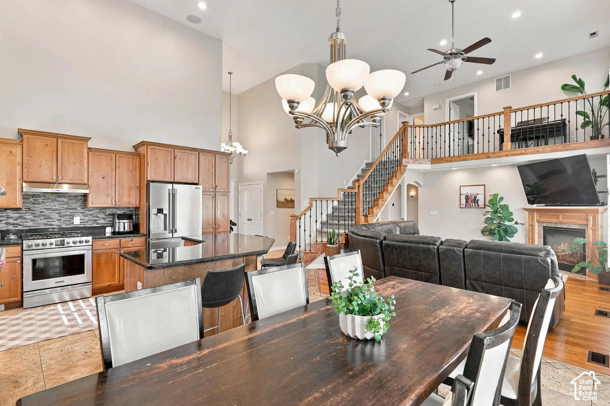 Open-concept living space featuring a two-story ceiling, kitchen island with seating, stainless steel appliances, a gas fireplace with a wood mantel, and an upper-level balcony