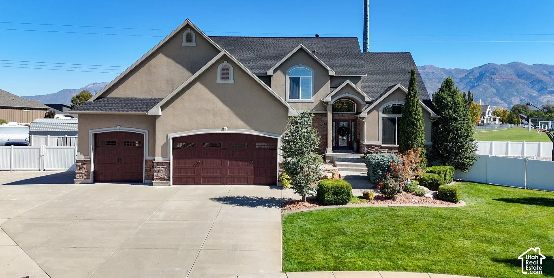 Stucco exterior with stone accents, dark wood-finish garage doors, concrete driveway, and front lawn with mature landscaping