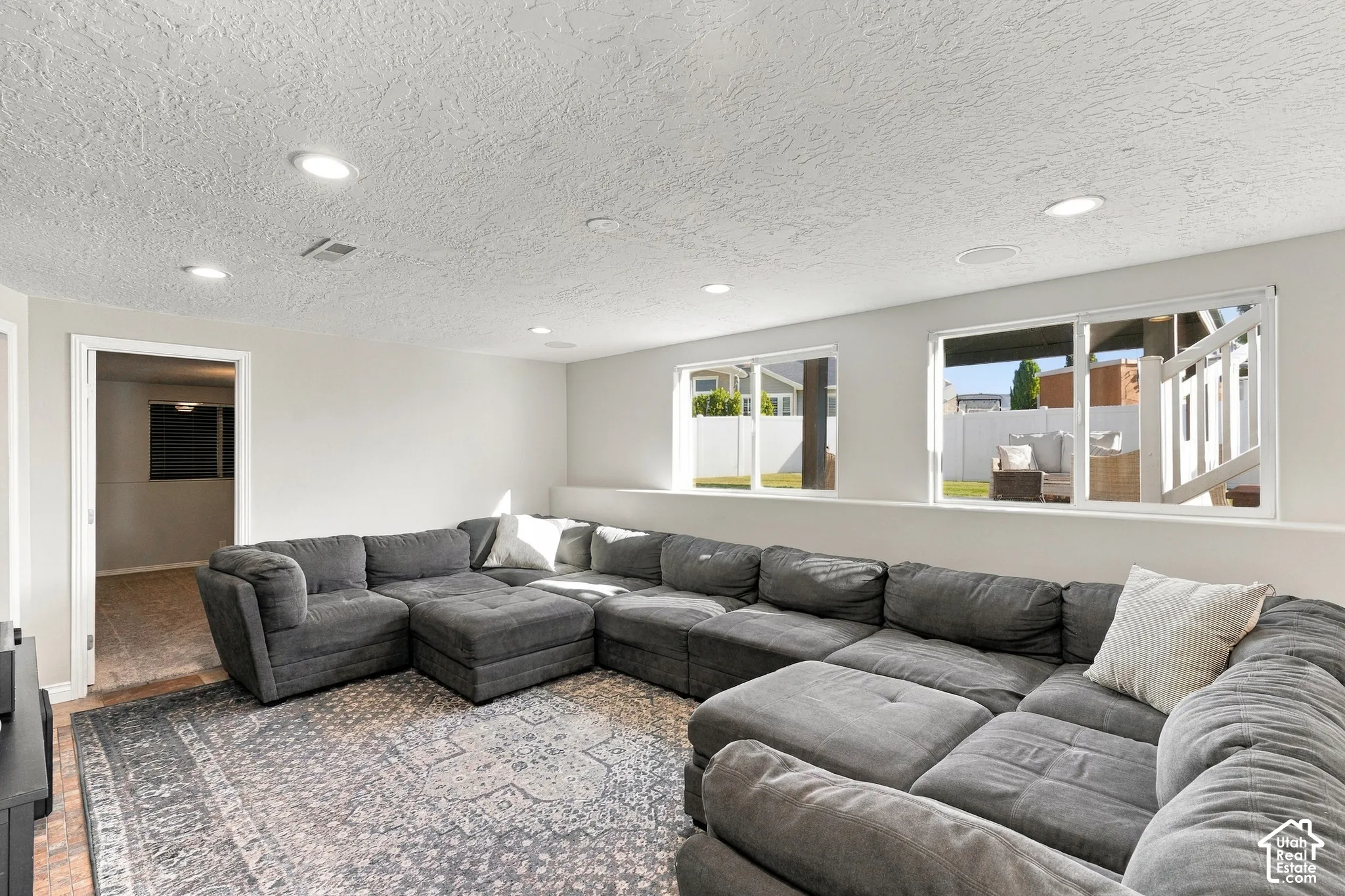 Recessed lighting illuminates this space featuring light gray walls, wood-finish flooring, and multiple windows