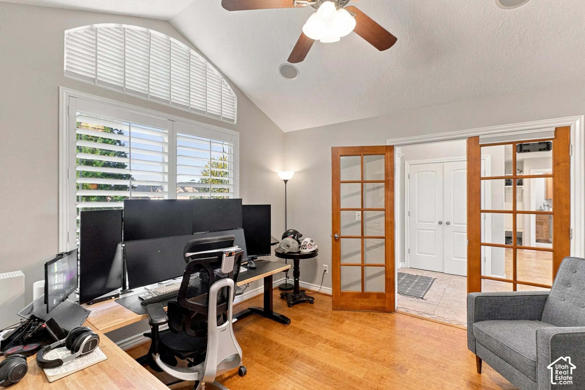 Vaulted ceiling with a ceiling fan, hardwood flooring, arched window with plantation shutters, French doors with glass panels, and recessed lighting
